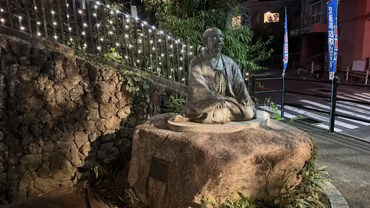 The Hideyoshi statue in Yukemuri Square at night, seated beside a stone wall.