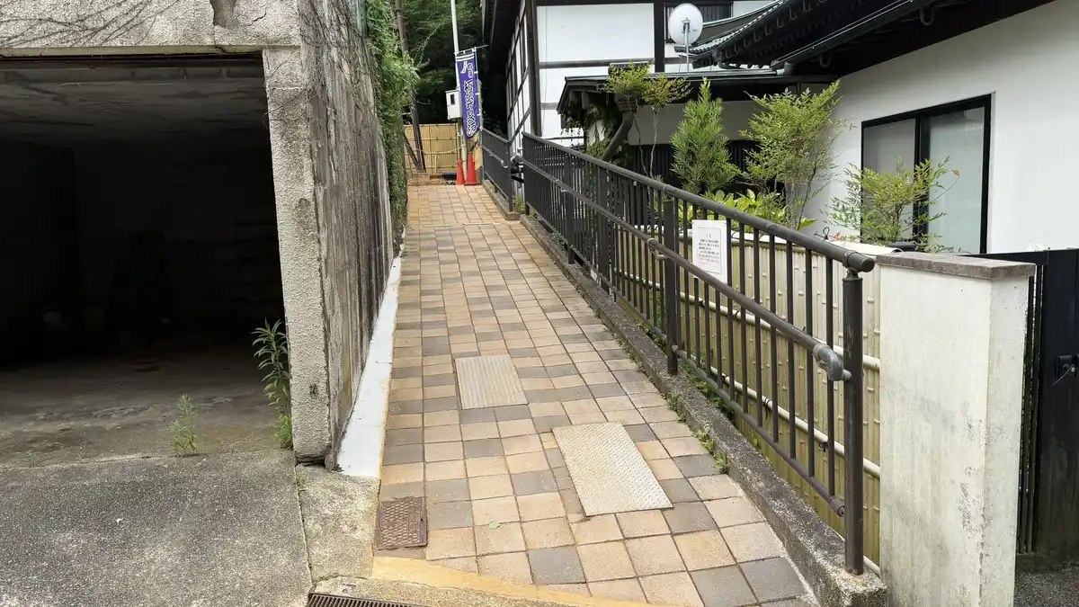 A stone-paved path with a handrail leading to the entrance to Gokuraku Spring.