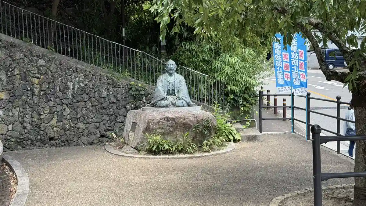 The statue of Toyotomi Hideyoshi in Yukemuri Square, seated beside a curving walkway and a stone wall.